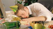 Young man asleep at desk, surrounded by remnants of office party